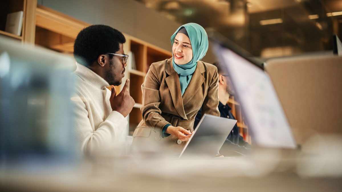 Woman leading a discussion with colleagues using a laptop in a modern office.