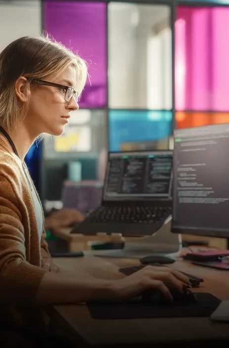 TP employee working on dual monitors with code displayed in a modern office. TP employee working on dual monitors with code displayed in a modern office.