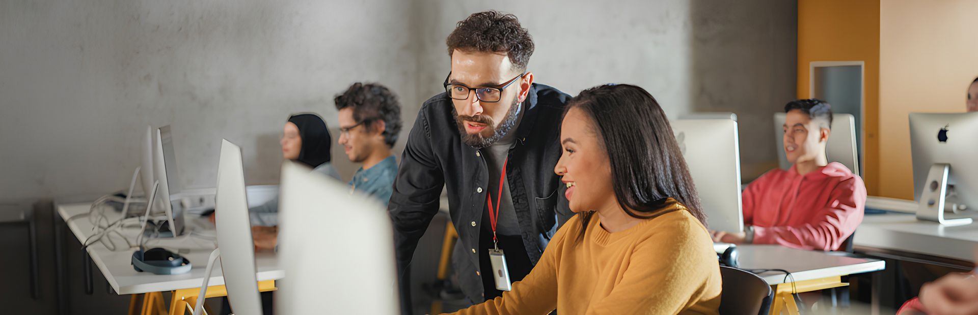 Young professional guiding a colleague on a computer in a collaborative workspace.