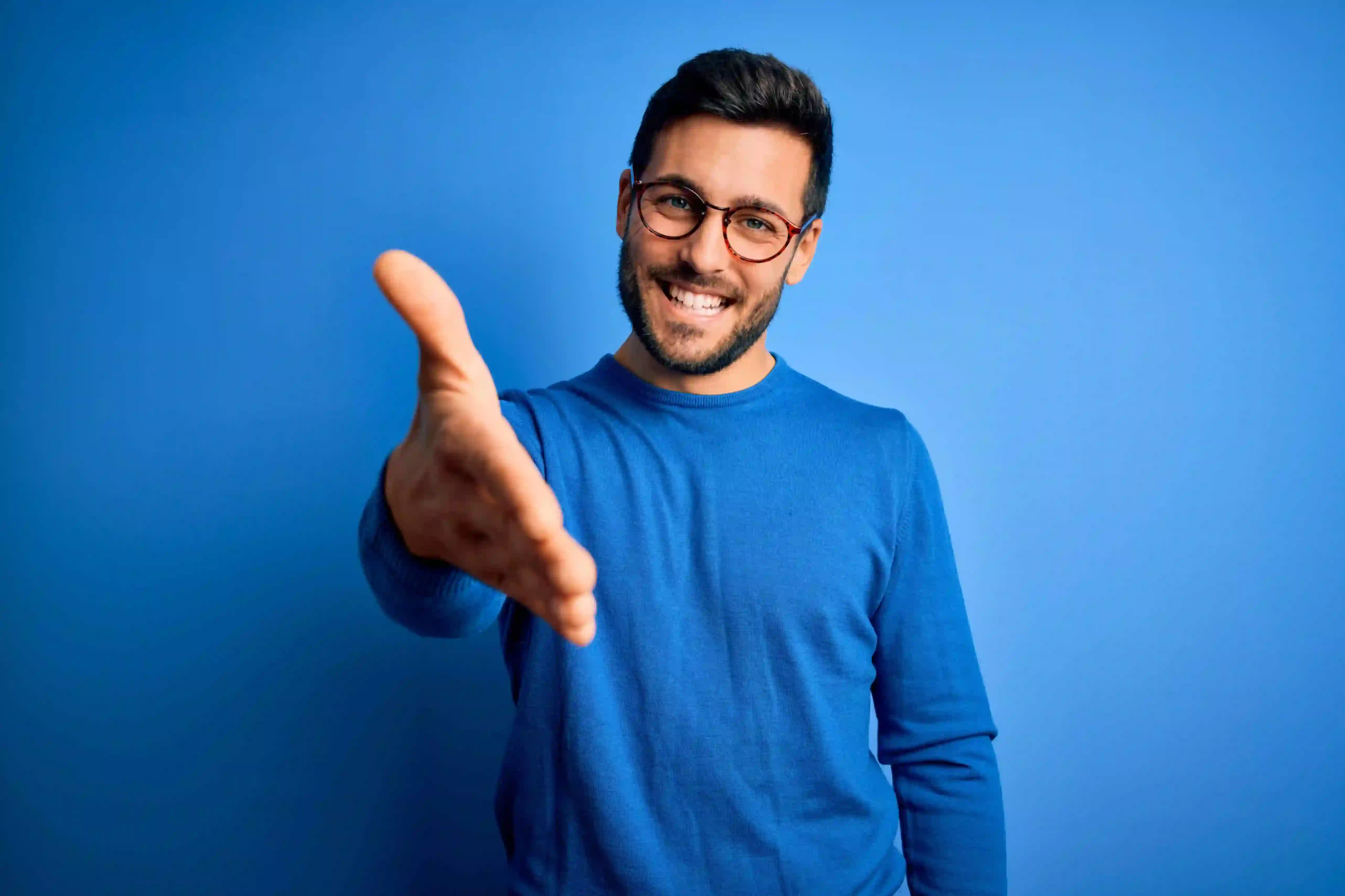 Smiling man in blue sweater offering a handshake, symbolizing a welcoming environment at TP.