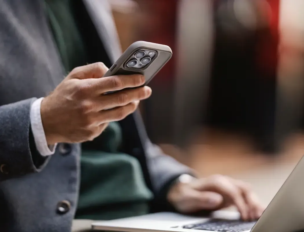A man in formal wear uses a smartphone outdoors, focusing on the device in his hands.