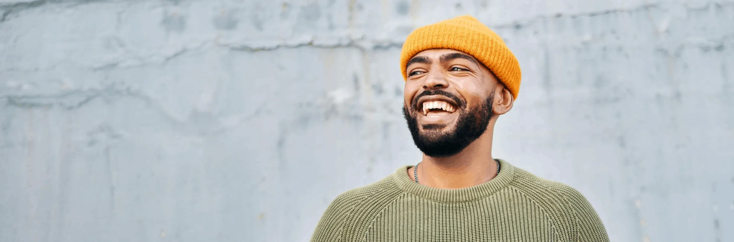 Smiling man with orange hat in front of a gray wall.