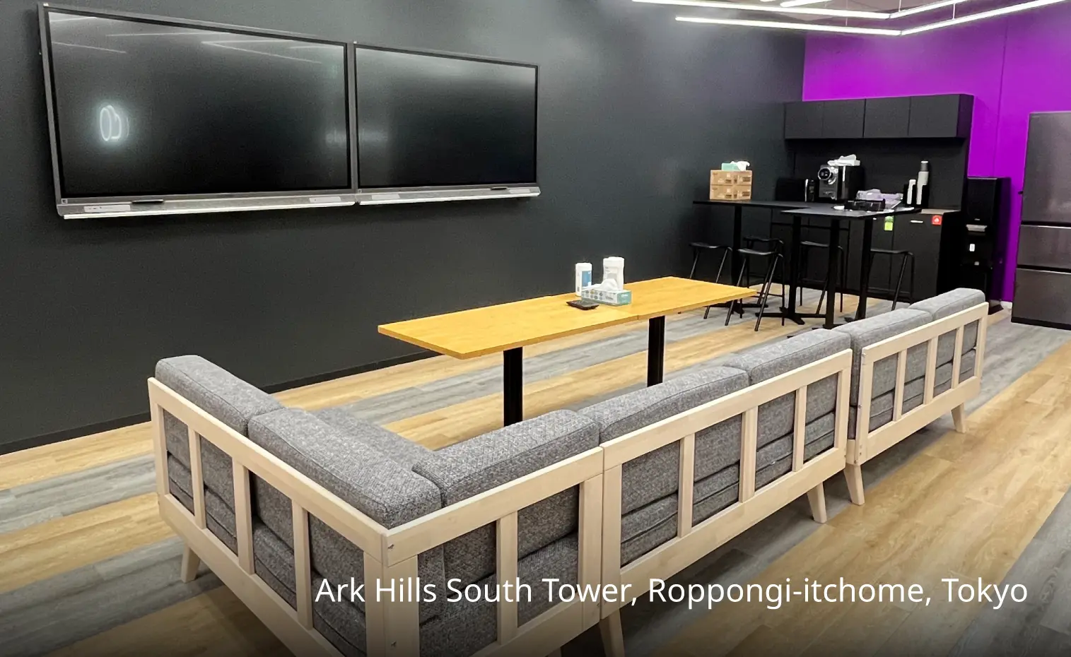 There is a sofa, a table, a sideboard and two wall-mounted TVs in the room.