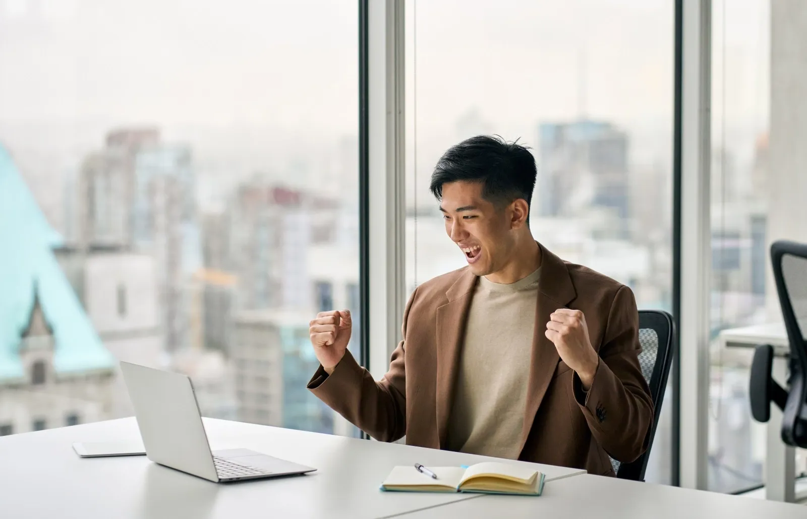 Man celebrating success while looking at a laptop in a modern office.