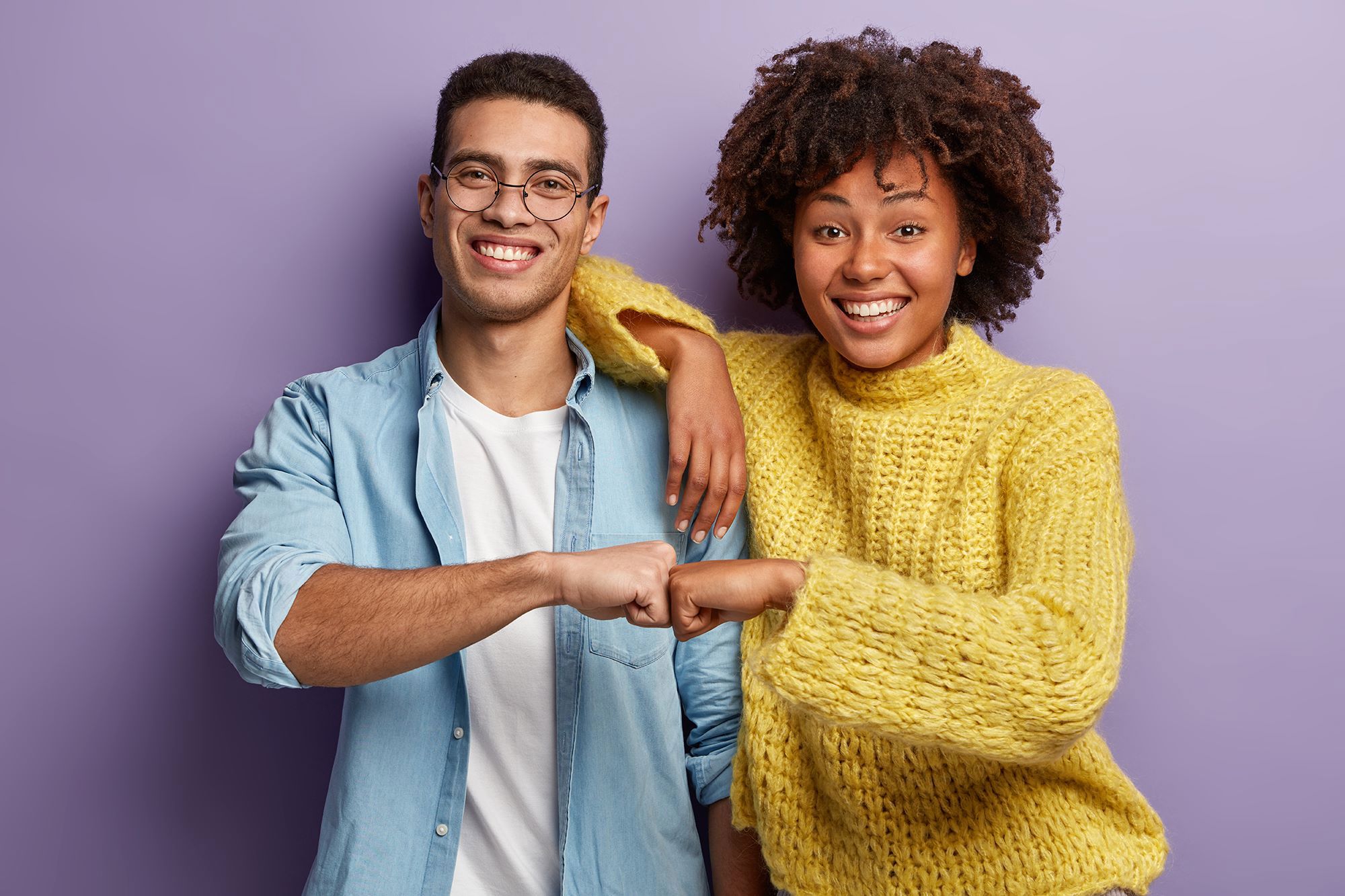 Two smiling people greeting each other with a fist bump against a purple background.