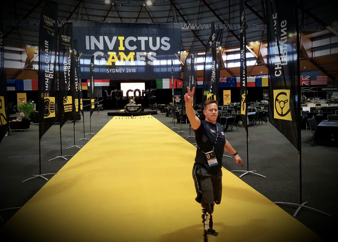 Para-athlete with prosthetic leg walking on yellow carpet at Invictus Games Sydney 2018, raising hand in victory gesture