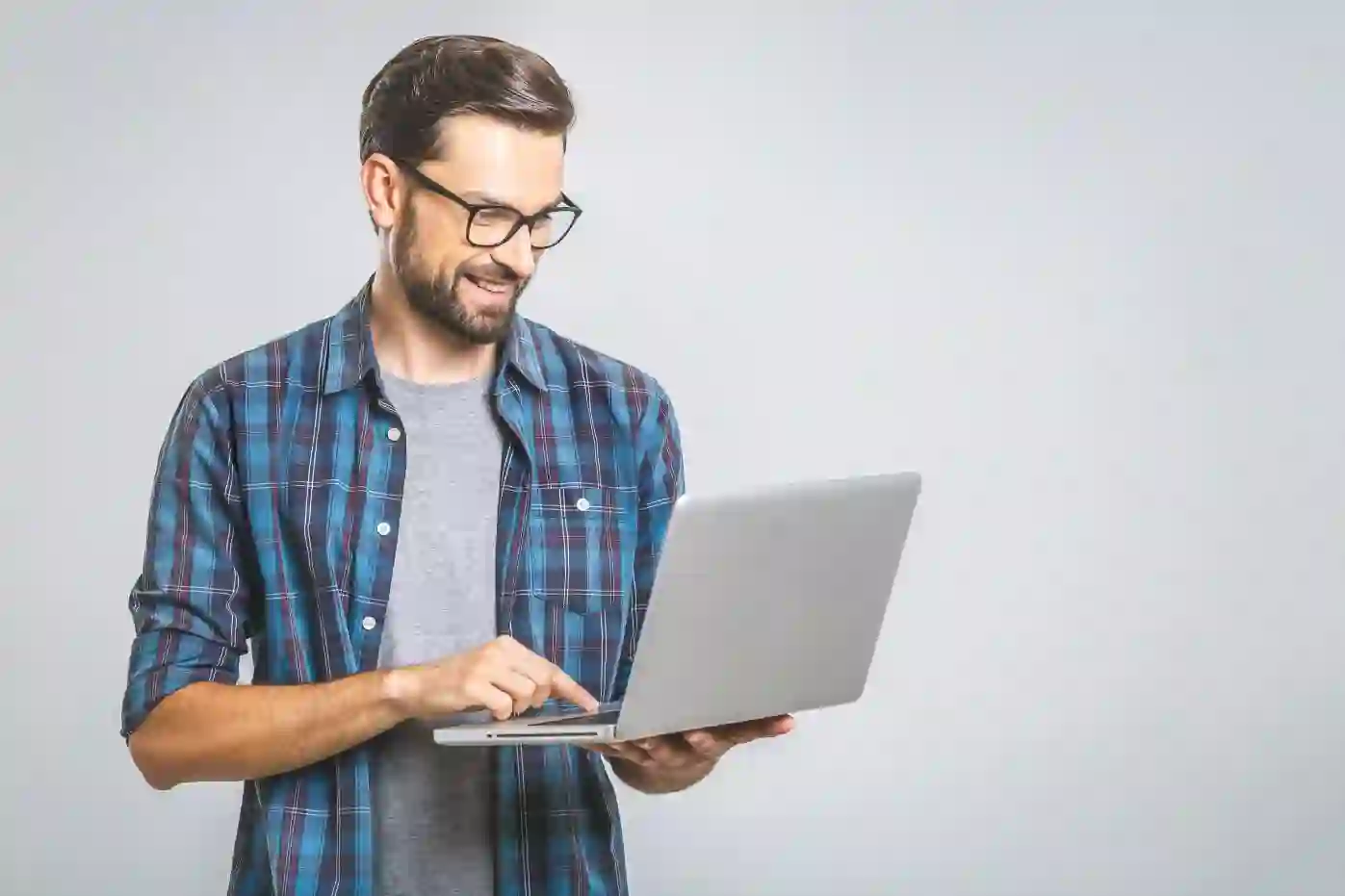 Smiling man with beard and glasses working on laptop in casual plaid shirt