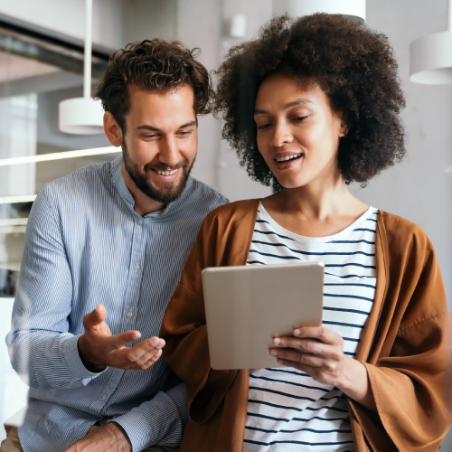 A woman holds a tablet, discussing content with a man gesturing next to her in a modern office space, featuring hanging lights and glass partitions.