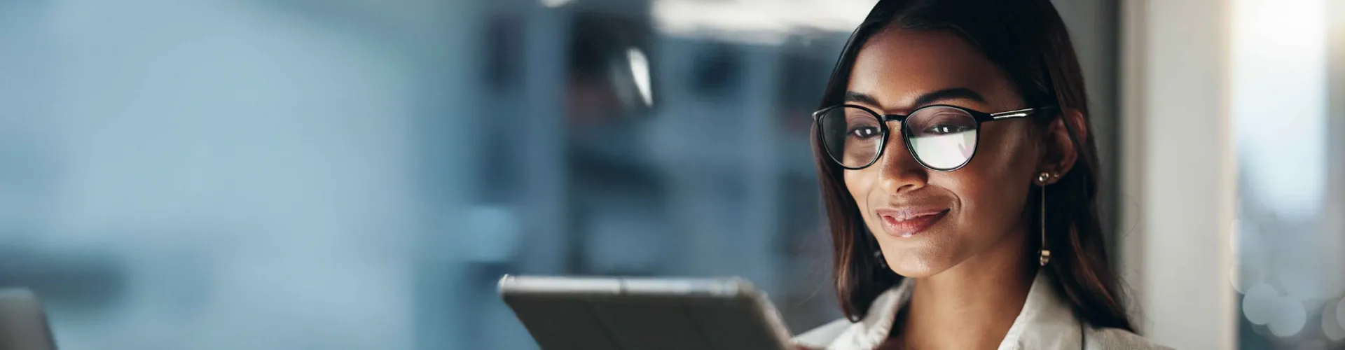 Woman wearing glasses smiling while working on a digital device.”