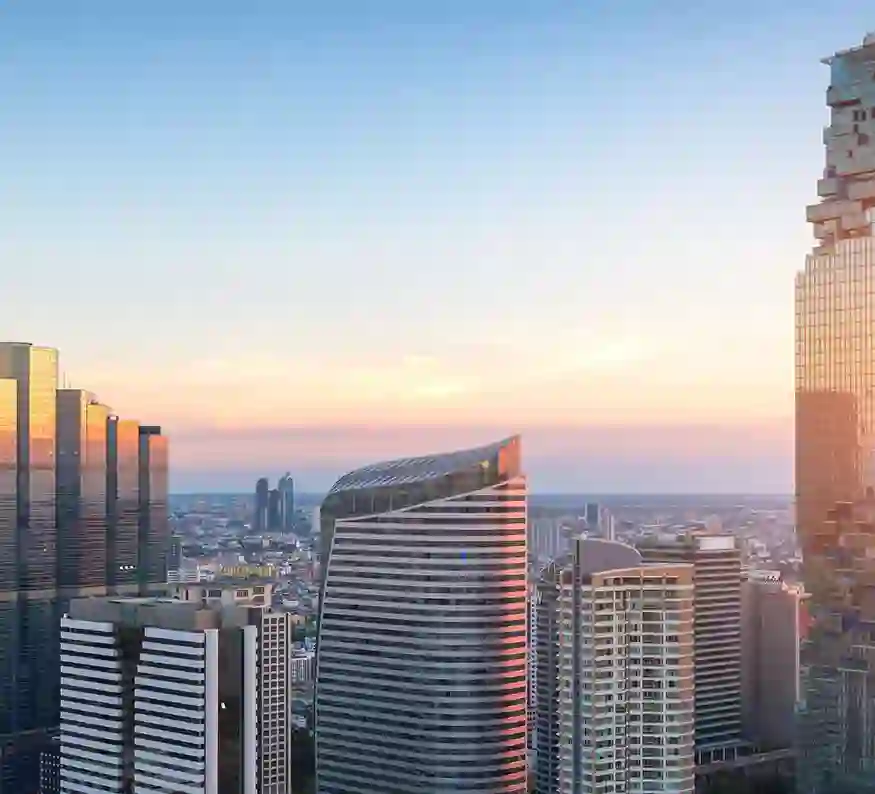 Skyscrapers at sunset with orange light reflecting on buildings under a gradient sky over the cityscape.