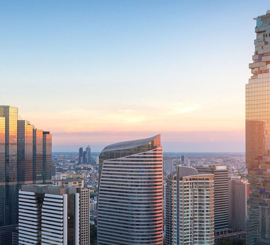 Skyscrapers at sunset with orange light reflecting on buildings under a gradient sky over the cityscape.