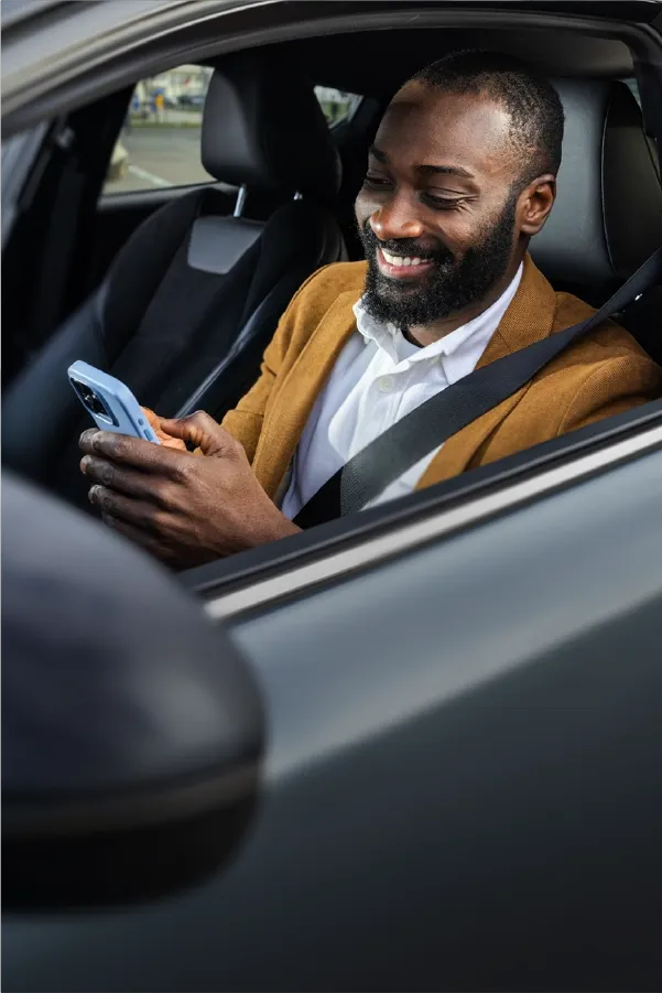 Smiling man using a smartphone while sitting in a parked car.