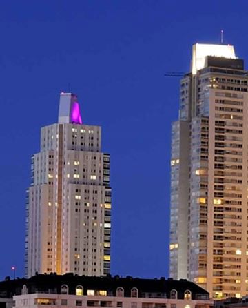Dos altos rascacielos se alzan iluminados contra un cielo azul profundo al atardecer.