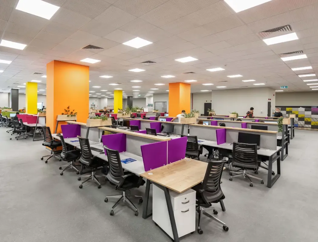 A bright, colorful open-plan office workspace with cubicles and desks.