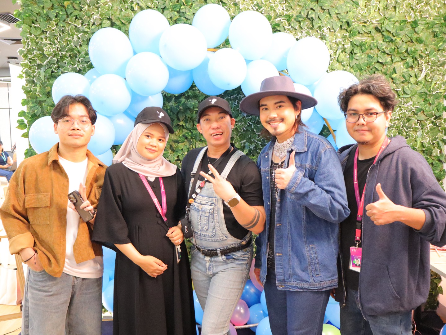 TP employees posing in front of blue balloon and greenery backdrop