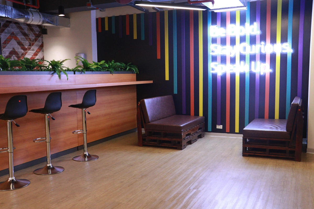 Colorful office lounge with bar stools, neon sign and pallet seating.