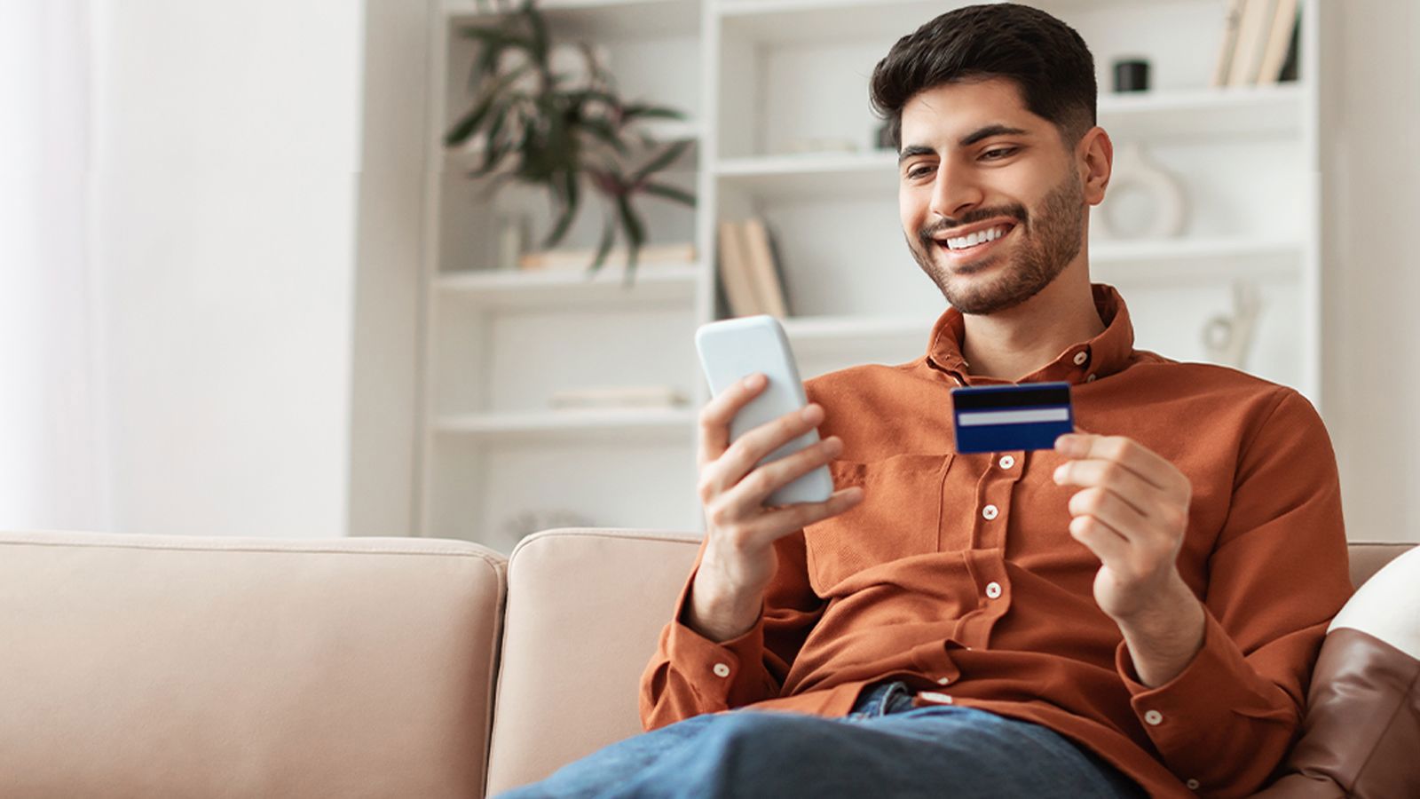 TP customer smiling while using a smartphone and credit card for an online purchase at home.