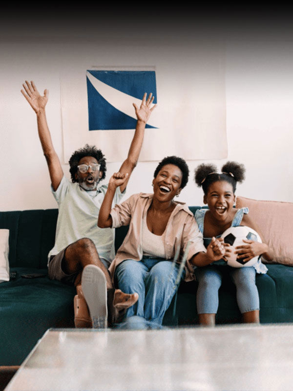 Three people sit on a couch, joyfully celebrating while watching something, in a living room