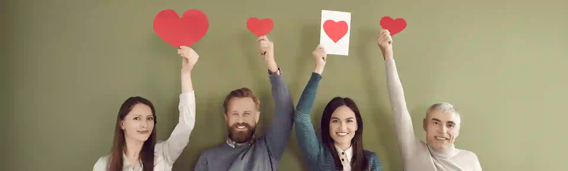 Group of smiling people holding up red paper hearts against a green background.