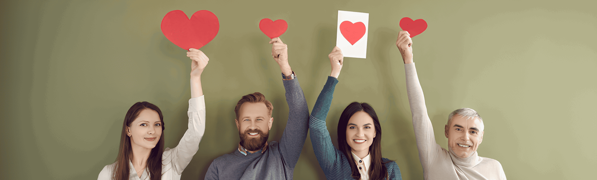 Group of smiling people holding up red paper hearts against a green background. Group of smiling people holding up red paper hearts against a green background.