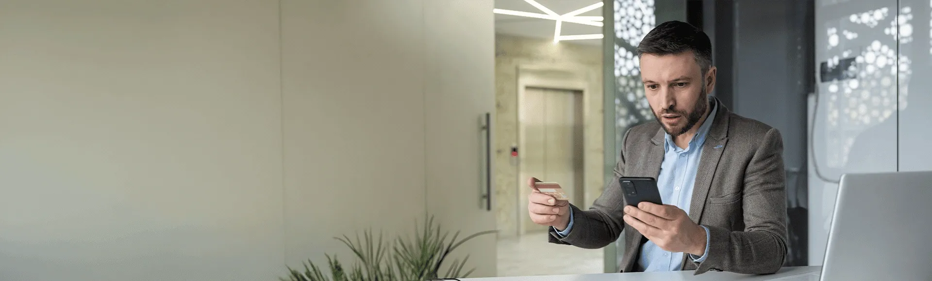 Man victim of financial crime looking at his cell phone in surprise while holding his credit card