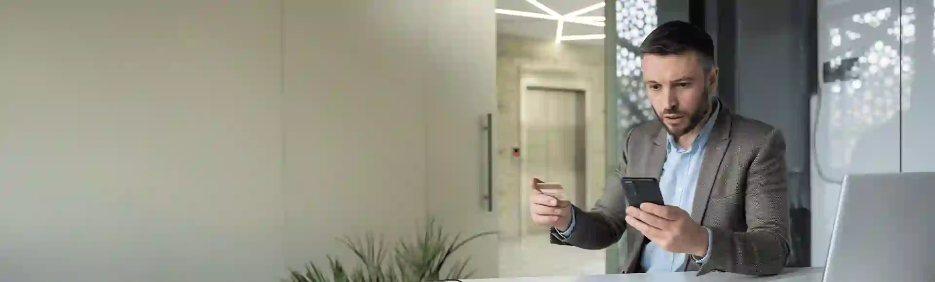 Man victim of financial crime looking at his cell phone in surprise while holding his credit card