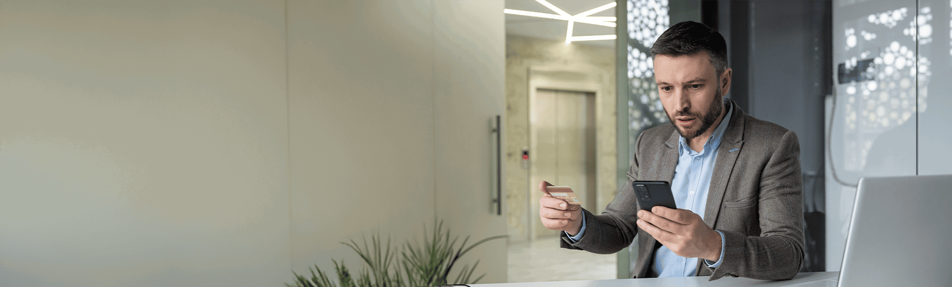 Man victim of financial crime looking at his cell phone in surprise while holding his credit card