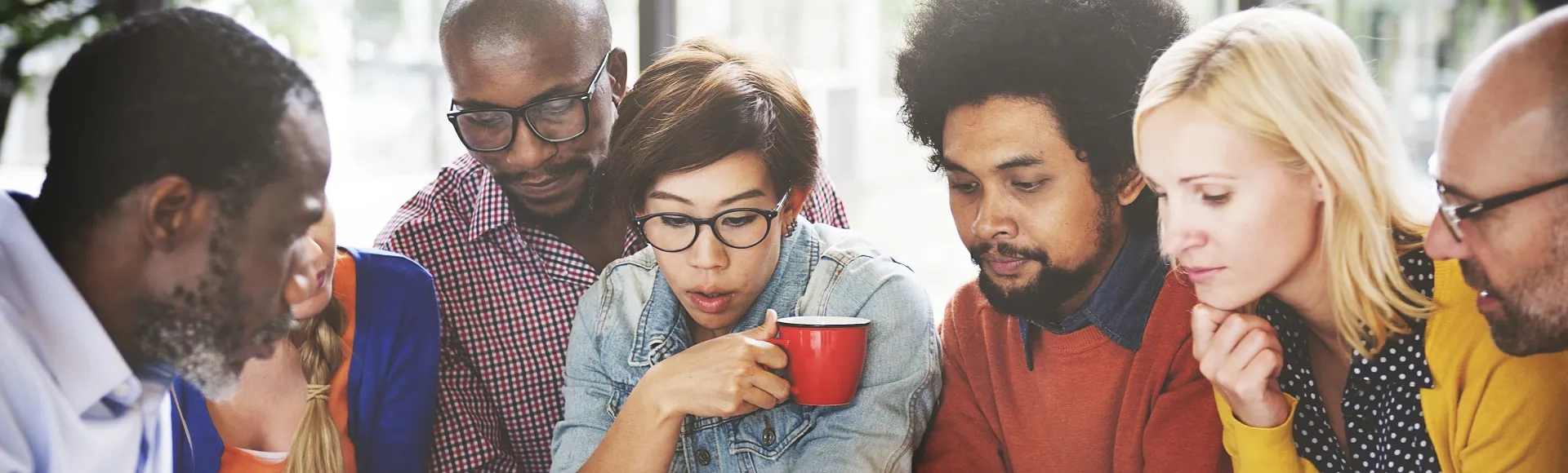 Group of colleagues gathered together, reviewing content and discussing ideas around a shared screen.