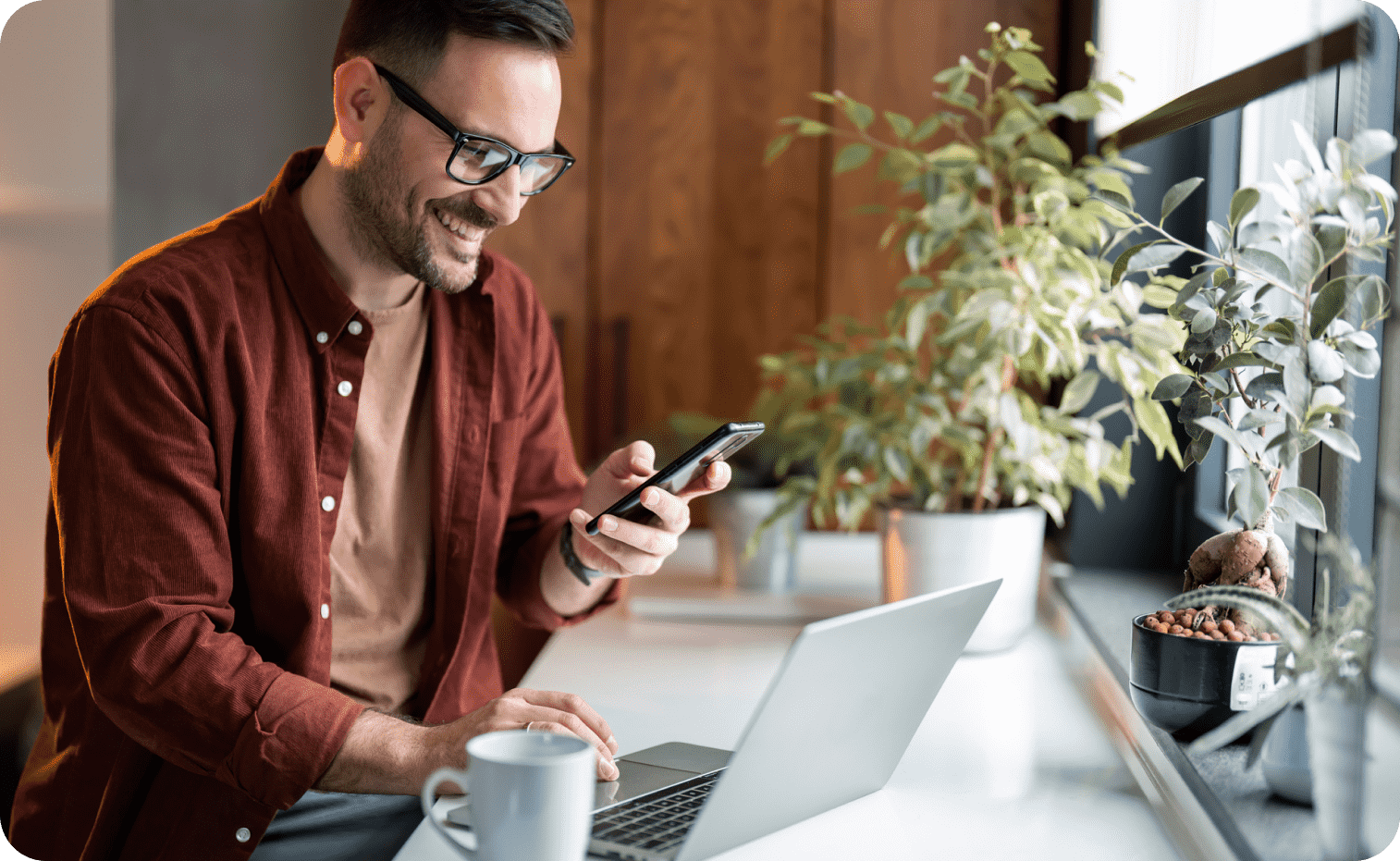Man looking at smartphone while working on laptop 