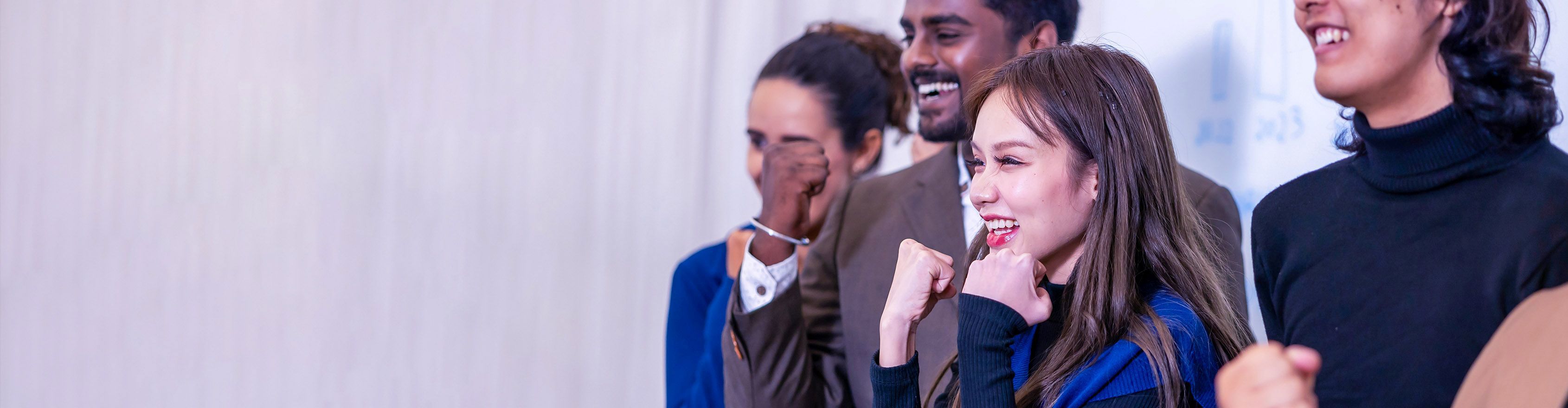 A diverse group of colleagues cheers enthusiastically, showing strong team spirit and excitement.