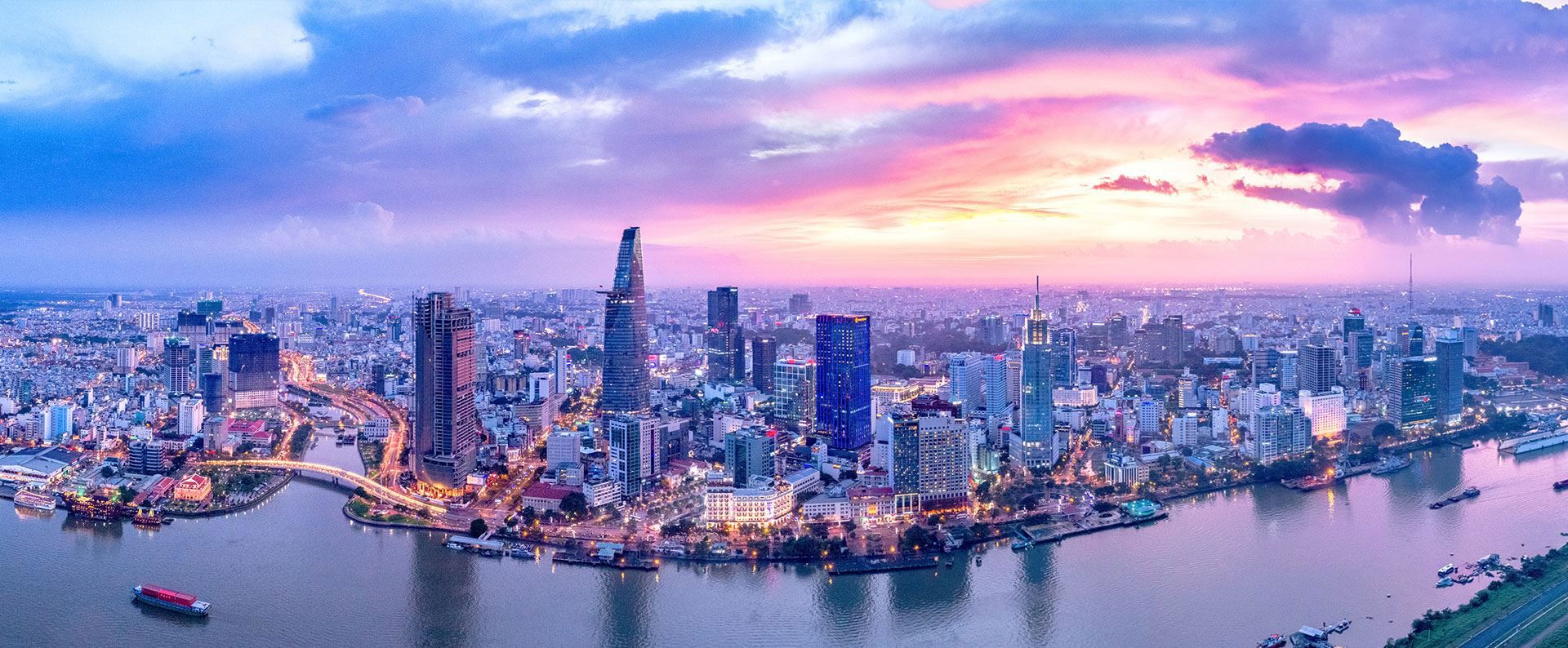 Skyscrapers rise densely, reflecting in a winding river during a vibrant sunset. the cityscape.