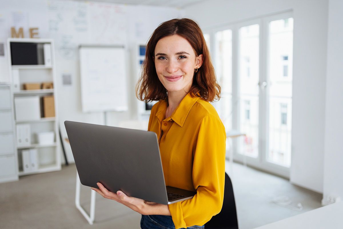 Smiling woman holding her laptop inside a white walls office