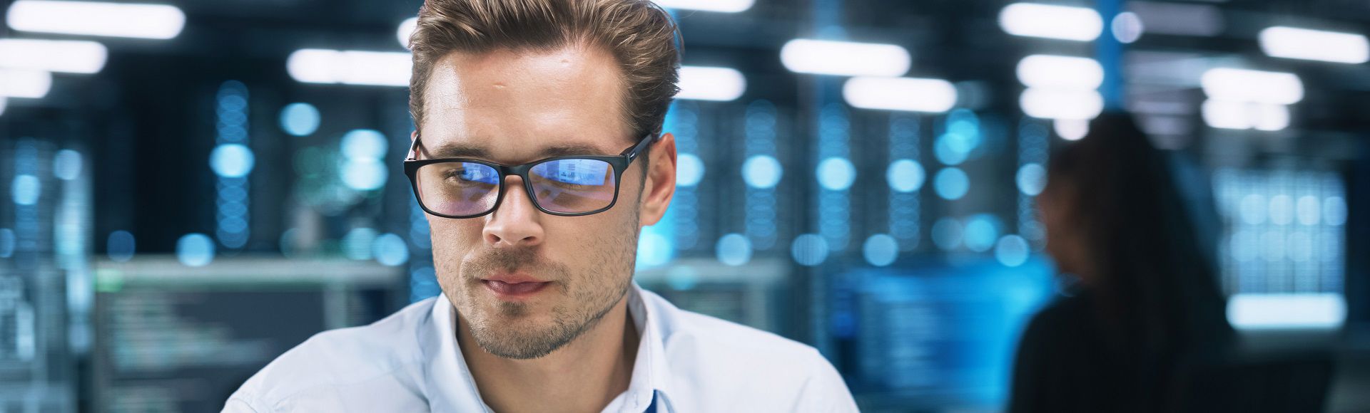 Man wearing glasses working inside a data center, surrounded by server racks and high-tech equipment.
