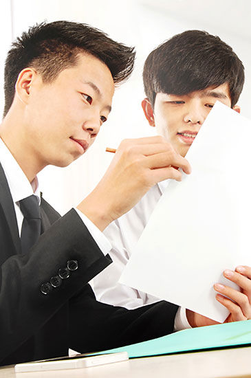 two people are examining and discussing documents. one holds the papers and points, while the other listens attentively. 