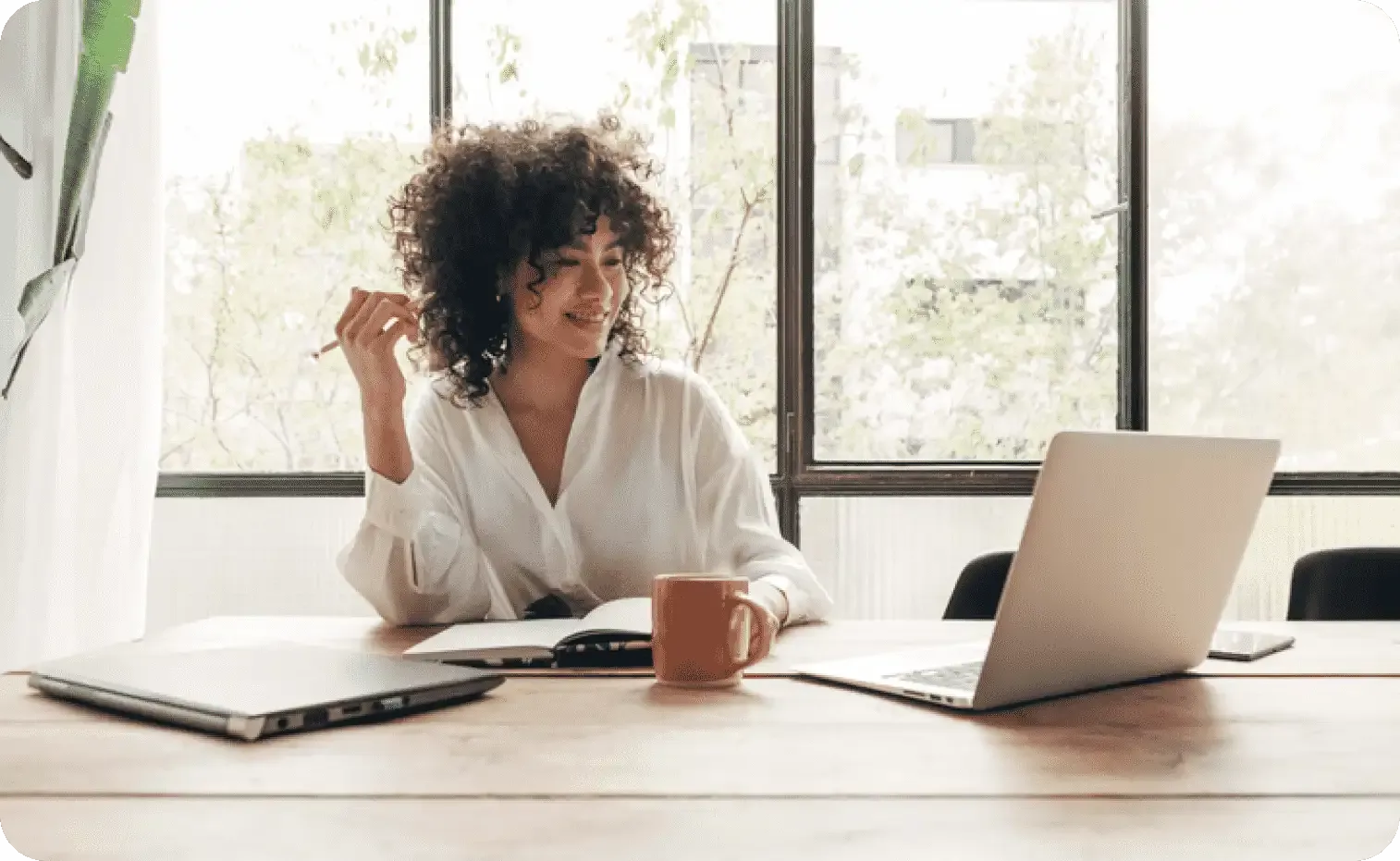 Young woman on a bright office reading a book while working on a laptop