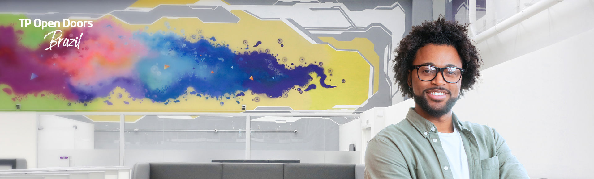 TP Open Doors Brazil event with a smiling man in front of a colorful mural in a modern office space.