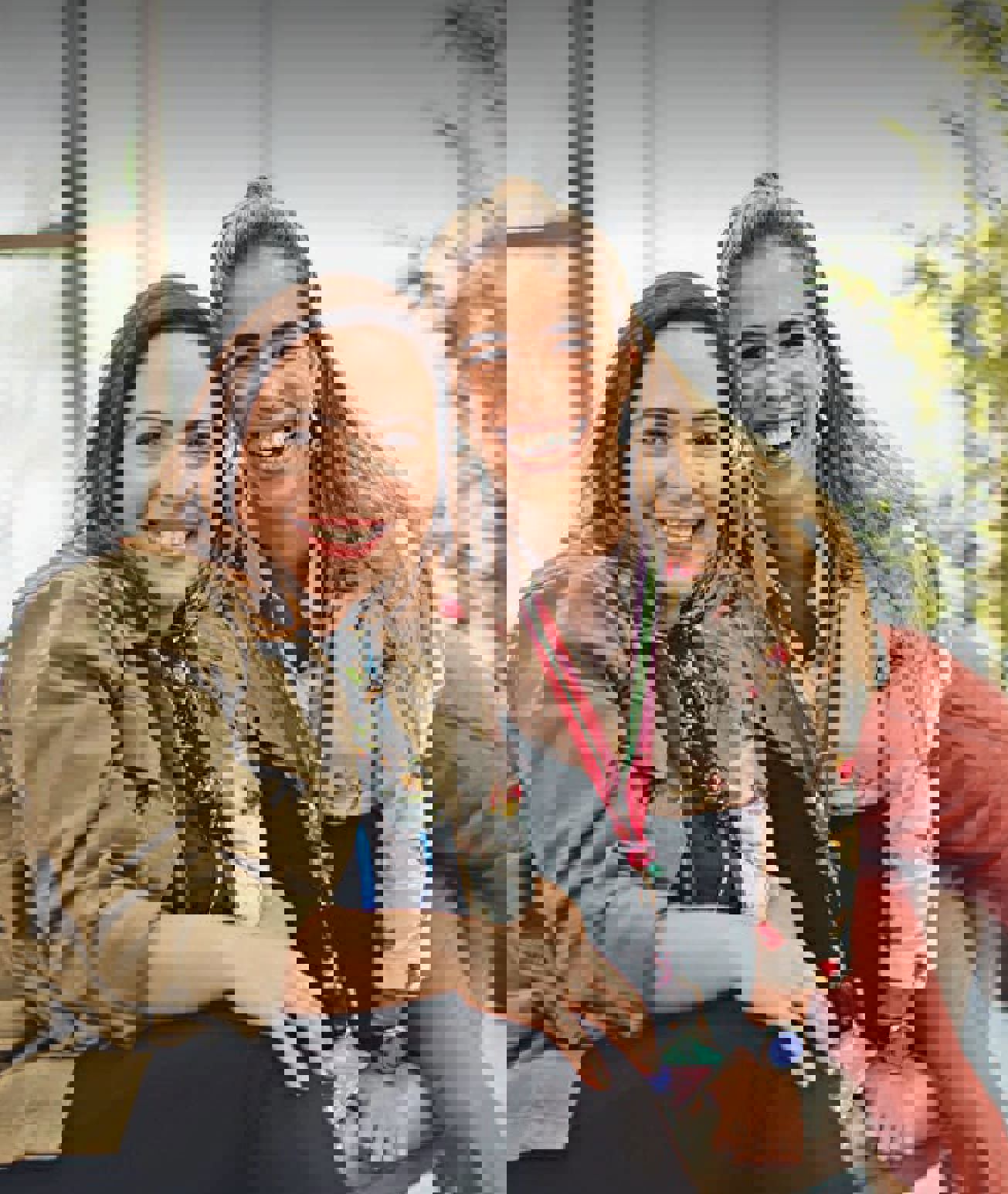 Two women smiling while sitting outdoors, one wearing a green jacket and the other in a red outfit.