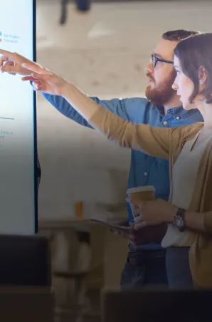Two colleagues reviewing charts on a large screen during a collaborative work session.