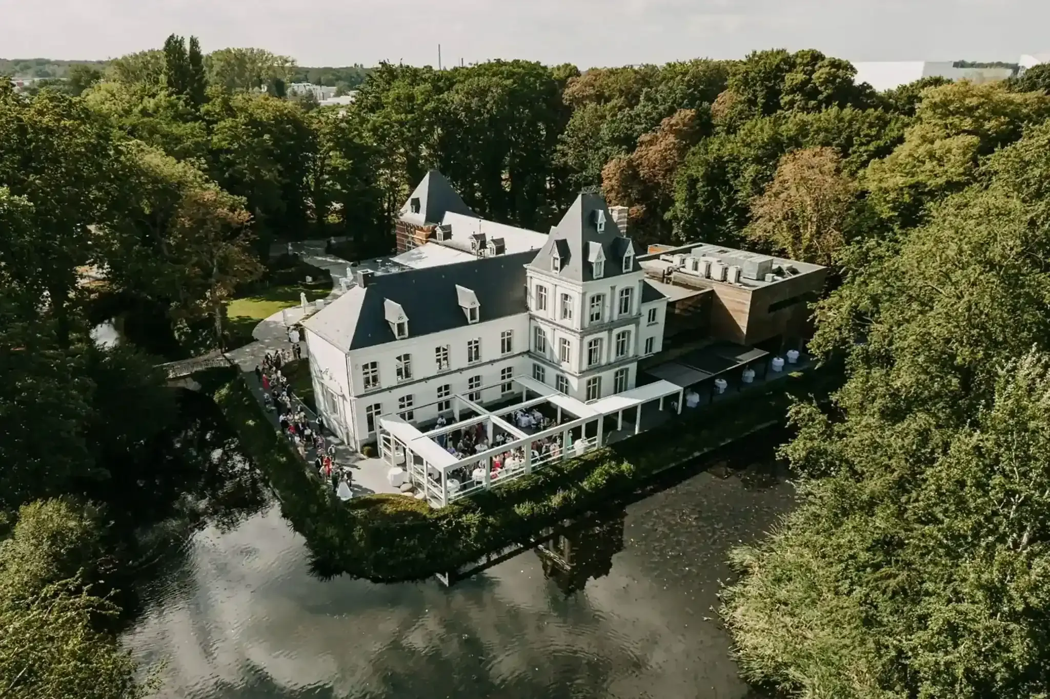 A big white house circled by a lake and a forest.