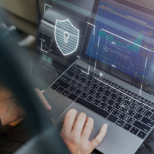 Uma pessoa digita em um laptop que exibe ícones de segurança digital, incluindo um escudo com um cadeado, em um ambiente de alta tecnologia com gráficos de dados na tela.