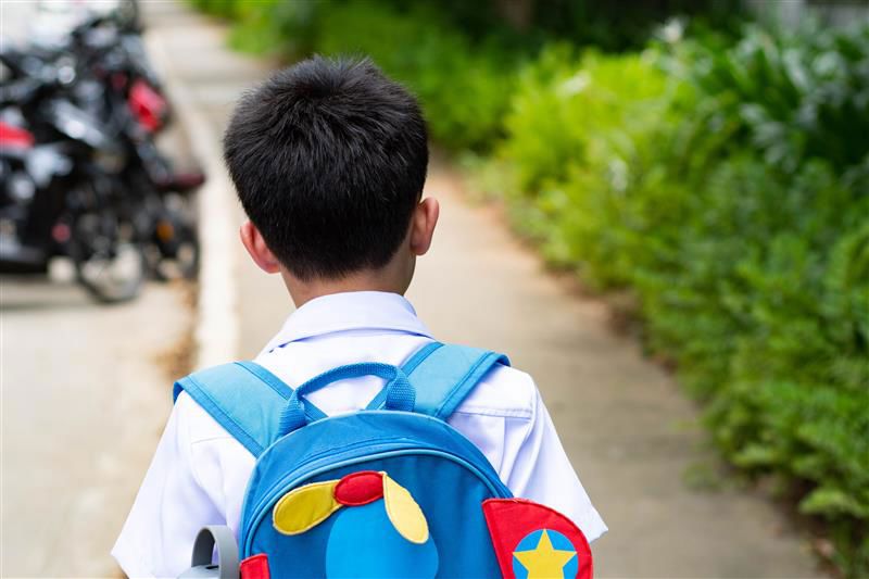 Boy walking on a sidewalk with a blue backpack, seen from behind.