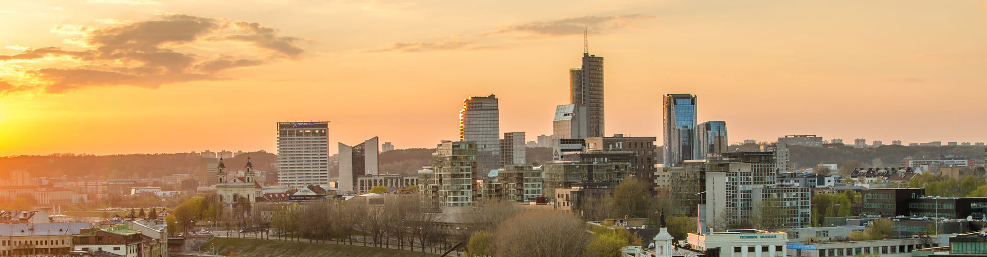 City skyline of Vilnius, Lithuania at sunset with modern skyscrapers and warm sky in the background.