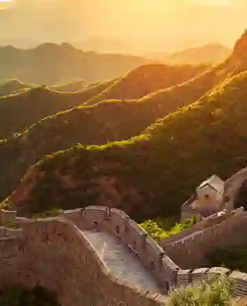 夕阳下的长城蜿蜒穿过绿色山脉，石塔在金色的光线中显得格外突出。