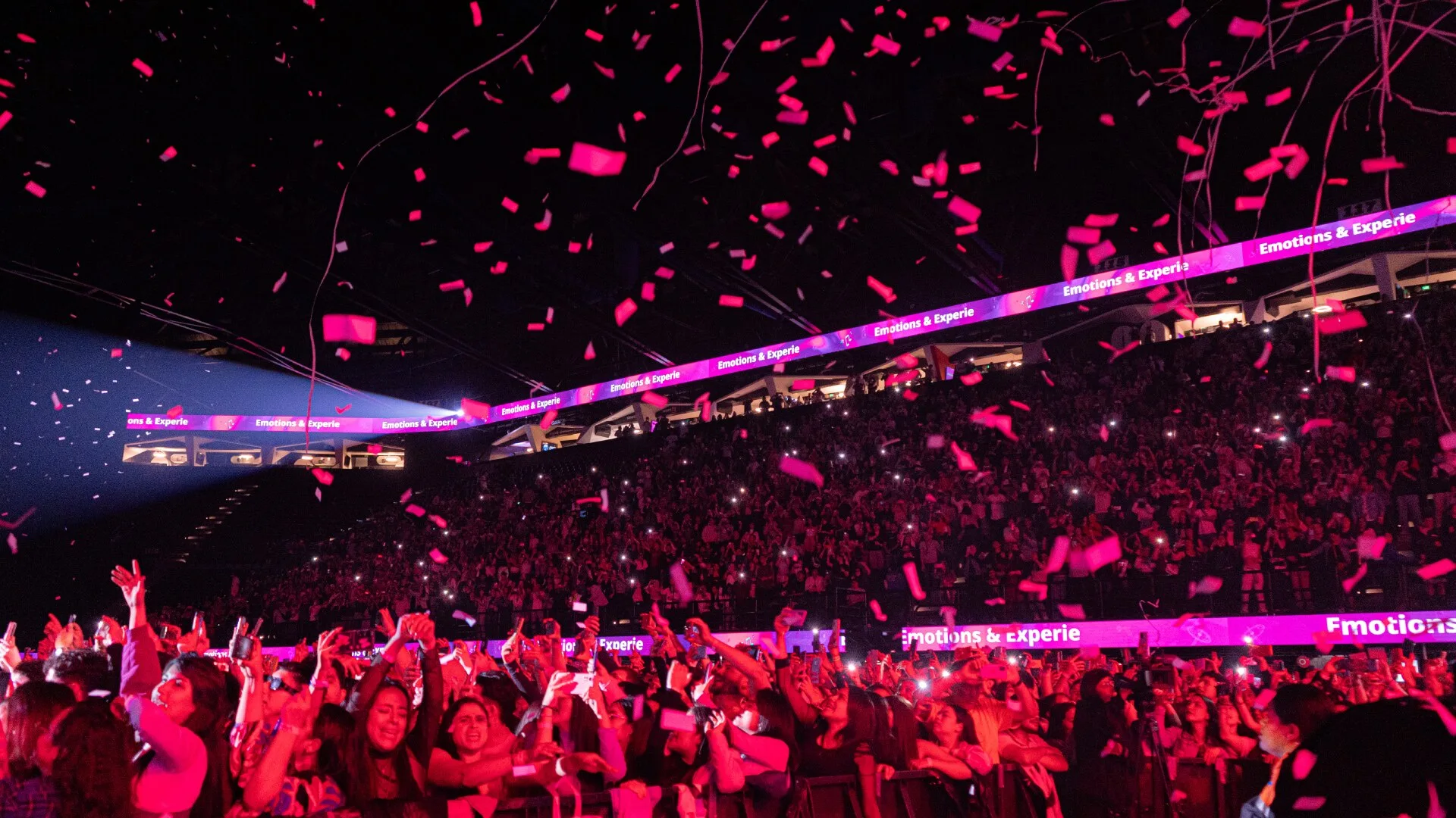 A crowd of people in a party with pink shredded paper falling from the ceiling.