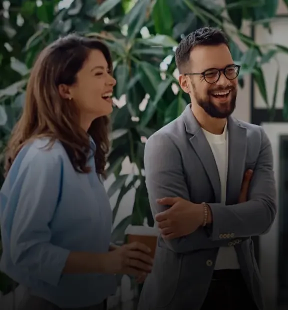 Group of employees talking and laughing in a modern, tree-lined office