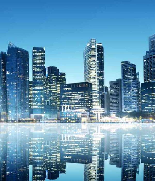 Skyscrapers at dusk reflected on calm water with illuminated windows and clear evening sky.