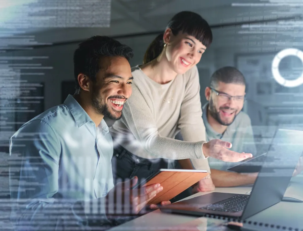 Three colleagues are having a work discussion by the computer: a female team member smiles and gestures to explain the on-screen content, and the two male colleagues look on with smiles.