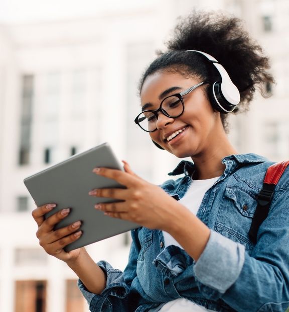 Giovane donna afrodiscendente sorridente ascolta musica all’aperto con un headset.