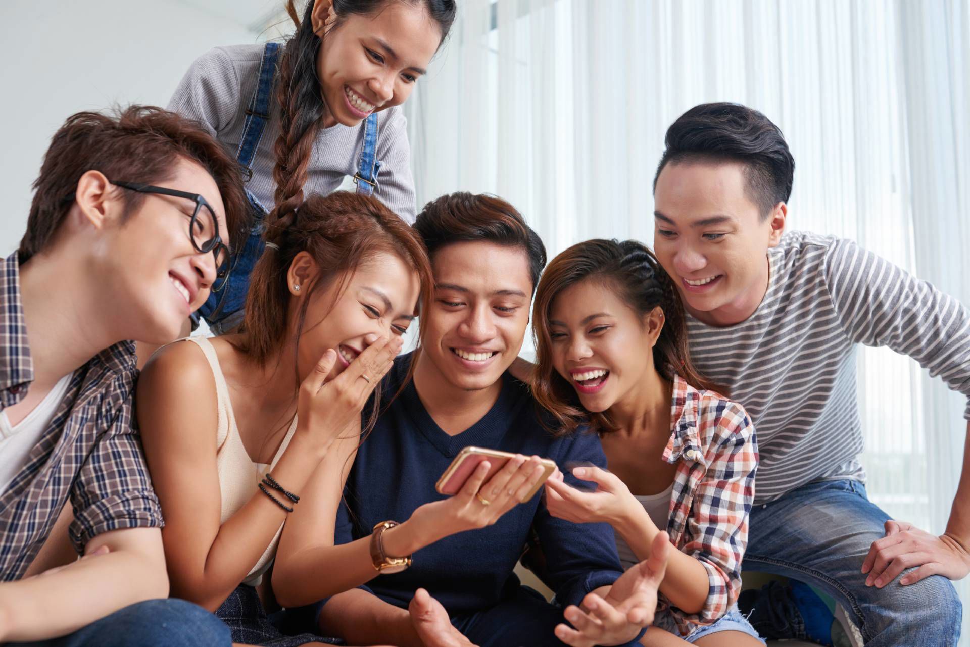 Group of friends smiling and laughing while looking at a smartphone together.