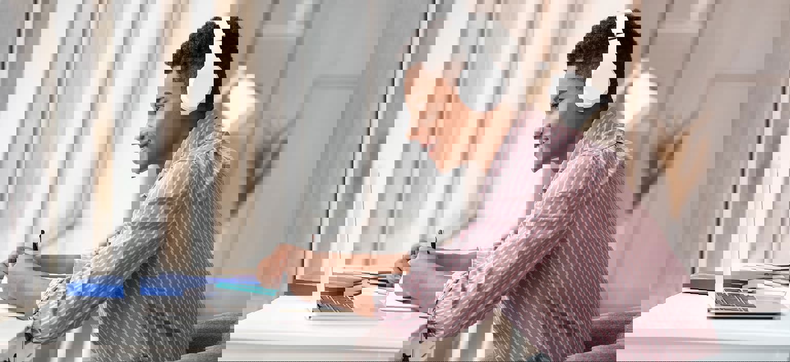 a man sat at desk with a laptop open, whilst wearing headphones and writing in a book a man sat at desk with a laptop open, whilst wearing headphones and writing in a book